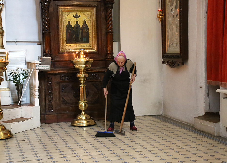 old lady sweeping church in Pskov, Russia
