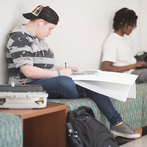 Student drawing on a bench in the hallway of Edwards College of Arts & Humanities
