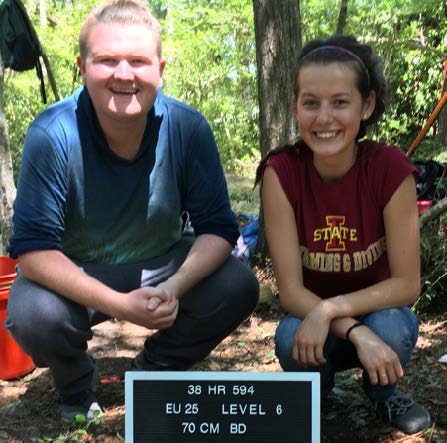 Students sitting near dig marker during field work.