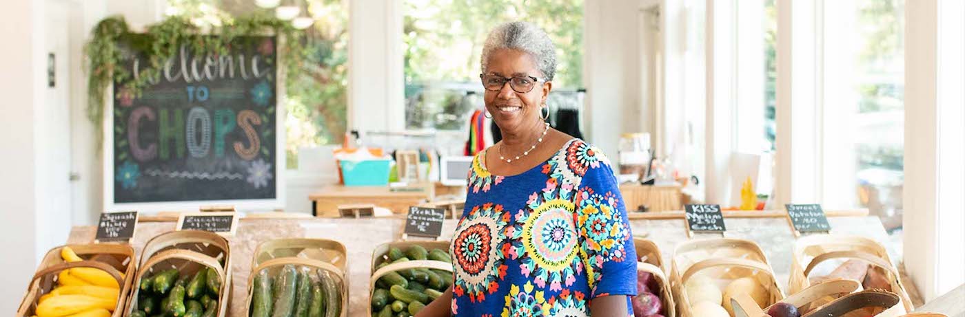 A woman with grey hair stands in front of colorful produce at CHOPS community kitchen in Conway, SC.
